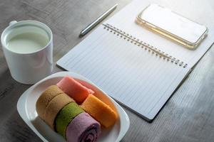 notizbuch, smartphone, marmeladenrolle, tasse milch, stift auf holz, geschäft, bildungskonzept und design foto