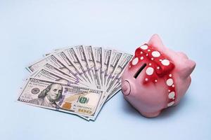 Geld aufgefächert neben einem Sparschwein auf blauem Grund foto