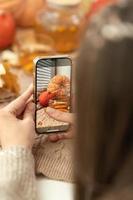 Mädchen, das Foto von Kürbissen, Herbstlaub und Teekanne auf einem Fenster macht. Mädchen fotografiert am Telefon rustikale Halloween-Komposition. Frohes Erntedankfest und Halloween