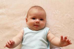 Porträt eines lächelnden dreimonatigen Babys im blauen Body liegt auf einer beigen Decke und schaut in die Kamera. foto