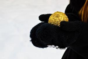 schöne festliche elegante gelbe, goldene runde kugeln, weihnachtsschmuck für das neue jahr, weihnachten liegt in den händen in schwarzen handschuhen vor dem hintergrund des weißen schnees im winter foto