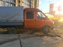 Auf dem Boden steht ein Lastwagen mit einem orangefarbenen Fahrerhaus und einem grauen Sockel. ein Auto mit kleinen Rädern zum Transport von Gütern. Transport von Baustoffen, Sand und Gütern foto