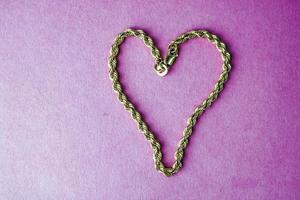 Textur einer wunderschönen goldenen festlichen Kette einzigartiges Weben in Form eines Herzens auf einem rosa lila Hintergrund und Kopierraum. konzept liebe, heiratsantrag, ehe, st. Valentinstag foto