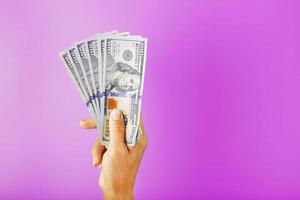 neue Dollarscheine in der Hand auf einem rosa Hintergrund. das Konzept der finanziellen Unterstützung. foto