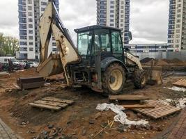 Baumaschinen befindet sich im Stadtzentrum in einer modernen Wohnanlage. ein traktor mit sandeimer steht neben anderen maschinen auf dem hof. Bau von neuen Wohngebäuden foto