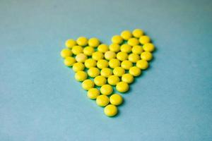 kleine medizinische pharmazeutische runde gelbe pillen, vitamine, drogen, antibiotika in form eines herzens auf blauem hintergrund, textur. konzeptmedizin, gesundheitswesen, herzerkrankungen. flache Lage, Draufsicht foto