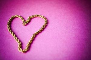 Textur einer wunderschönen goldenen festlichen Kette einzigartiges Weben in Form eines Herzens auf einem rosa lila Hintergrund und Kopierraum. konzept liebe, heiratsantrag, ehe, st. Valentinstag