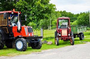 zwei rote professionelle landwirtschaftliche Bautraktoren mit großen Rädern mit Lauffläche zum Pflügen des Feldes, des Landes, des Warentransports foto