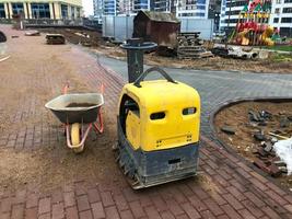 Maschine zur Herstellung von Beton und Pflaster für die gelbe Straße auf einer Baustelle. In der Nähe befindet sich ein Wagen für den Transport von schweren Materialien und Sand. Bau einer neuen Wohnanlage foto