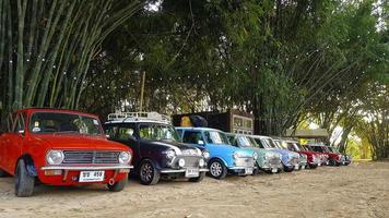 nakhon nayok, thailand - 5. dezember 2020 viele austin mini cooper oder klassische autos parkten auf der straße mit bambuswald und haus- oder heimhintergrund mit kopierraum. Gruppe von Oldtimern oder Retro-Fahrzeugen. foto