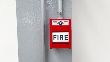 roter Feueralarmknopf zum Herausziehen im Notfall passiert in Stall auf grauem oder grauem Stahlmast mit weißem Wandhintergrund und Kopierraum. Warnausrüstung oder Werkzeug. foto