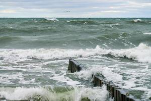 Blick auf das blaue Meer mit schäumenden Wellen und hölzernen Wellenbrechern foto