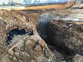 Sandgraben auf einer Baustelle. viel Sand, eine Grube mit Schutt und Steinen wurde ausgehoben. in der Nähe sind Holzleitern und Stöcke. Es gibt neue Häuser in der Nähe, die Kommunikation wird in der Grube verlegt foto