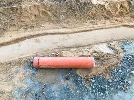 Ovaler orangefarbener Metallstab liegt auf dem Sand. Die Metallstruktur fiel von der Baumaschine. das Ersatzteil liegt auf der Baustelle. Dreck und Steine liegen auf dem Boden foto