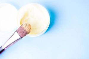 eine Beauty-Box mit einem Holzpinsel aus natürlichem Hartfussel für einen Ton und ein rundes Cremetiegel, eine Make-up-Basis mit Zweite-Haut-Effekt auf blauem Grund. flach liegen. Ansicht von oben foto