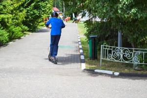 Ein Junge, ein Mann fährt auf einem neuen modernen Elektroroller mit Batterien die Parkstraße entlang und steht mit zwei Beinen darauf foto