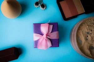 Schönheitsbox, loses mattes Mineralpuder und Rouge mit einem Schönheitsmixer für Make-up und silberne Ohrringe, Lippenstift und Geschenkbox auf blauem Hintergrund. flach liegen. Ansicht von oben foto