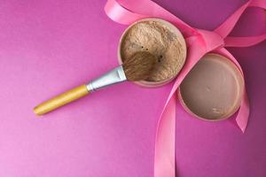 Schönheitsbox, bröckliger, matter Mineralpuder mit einem speziellen braunen, schönen Holzpinsel aus Naturflor für ein Make-up auf einem rosa-violetten Hintergrund mit einem zarten Satinband. flach liegen. Ansicht von oben foto