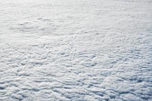 über den wolken draufsicht aus dem flugzeugfenster, dicke weißblaue wolken sehen aus wie weicher schaum foto