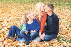 Porträt einer jungen Familie, die im Herbstlaub sitzt foto