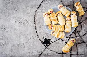 gruselige wurstmumien im teig mit lustigen augen auf dem tisch. lustige Dekoration. Halloween-Essen. Ansicht von oben. flach liegen foto