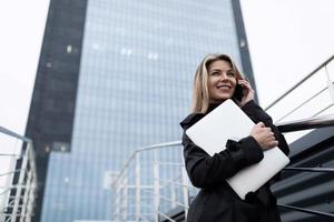 Porträt einer Geschäftsfrau vor dem Hintergrund einer Nichtglasfassade eines Bürogebäudes mit einem Laptop in der Hand foto