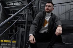 Porträt eines brutalen jungen Mannes, der auf der Treppe sitzt foto