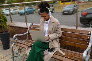 junge amerikanische vermarkterin, die an einem laptop außerhalb des büros arbeitet und kopfhörer trägt foto