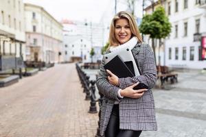 Porträt einer starken Geschäftsfrau mit Laptop und Handy in den Händen und einem Lächeln im Gesicht vor dem Hintergrund des Stadtpanoramas foto