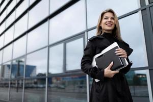 Porträt einer erwachsenen Frau einer erfolgreichen Führungskraft mit Laptop und Notizblock vor dem Hintergrund einer Glasfassade eines Bürogebäudes foto