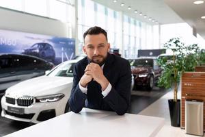 männlicher Geschäftsmann auf dem Hintergrund von Neuwagen im Autohaus, Konzeptautoversicherung foto