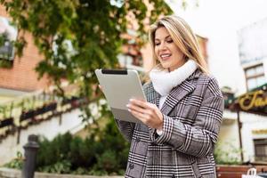 dünnere erwachsene Geschäftsfrau, die an einem Tablet vor dem Hintergrund eines Stadtgebäudes arbeitet foto