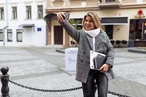 Stilvolle Frau in Herbstkleidung macht ein Selfie auf dem Hintergrund der Stadt foto