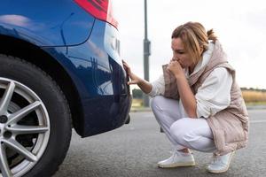 Verwirrte und verärgerte Frau, die nach einem kleinen Unfall einen Kratzer auf der Stoßstange des Autos ansieht foto