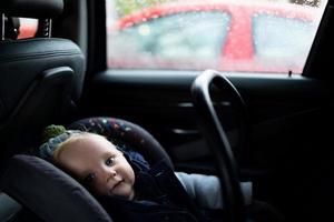 Baby sitzt in einem Auto in einer Trage, Foto mit Tiefenschärfe. Kindersicherheitskonzept