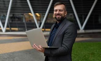 männlicher Wirtschaftsanalytiker mit einem Laptop auf dem Hintergrund eines Bürogebäudes foto
