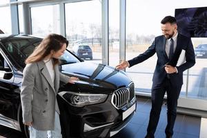 Eine junge Frau in einem Autohaus wählt zusammen mit einem Manager ein neues Auto aus, Mietwagenkonzept foto