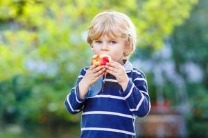 lustiger blonder Junge, der gesunden Apfel isst