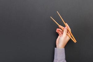 kreatives Bild von Holzstäbchen in männlichen Händen auf schwarzem Hintergrund. japanisches und chinesisches essen mit kopierraum foto