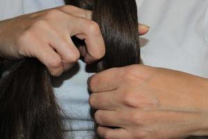 Ein Mädchen mit langen dunklen Haaren flechtet ihr Haar. Nahaufnahme Hände. Haarpflege. Problem mit Haarausfall. foto