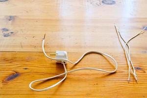 Weiße baumelnde elektrische Kabel mit einem elektrischen Stecker für eine Steckdose auf einem Holztisch foto