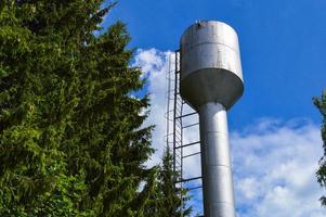 großer industrieller wasserturm aus eisenmetall glänzendem edelstahl zur versorgung von wasser mit großer kapazität, fass gegen den blauen himmel und bäume foto