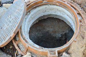 offener Abwasserkanal auf der Straße. Metalltunnel für die Wasserableitung, Schaffung eines Abwasserkanals. rostiger Schachtdeckel, Bauloch. Kanalisation auf der Baustelle. Produktion einer neuen Wohnanlage foto