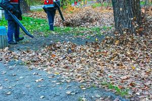 Arbeiter auf der Straße sammeln im Herbst Blätter mit einem Gebläse foto