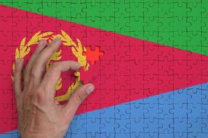 die eritrea-flagge ist auf einem puzzle abgebildet, das die hand des mannes zum falten vervollständigt foto