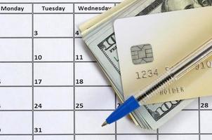 Stift und Kreditkarte auf vielen hundert US-Dollar-Scheinen auf Kalenderseite aus nächster Nähe foto