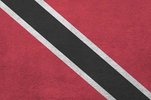 die flagge von trinidad und tobago ist in hellen farben auf einer alten reliefputzwand dargestellt. strukturierte Fahne auf rauem Hintergrund foto