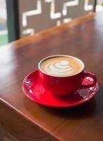 Nahaufnahme rote Kaffeetasse mit Herzform Latte Art auf Holztisch foto
