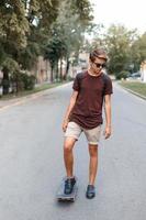 junger gutaussehender kerl mit sonnenbrille, der auf einem skateboard fährt. foto