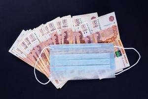 Geld und medizinische Maske auf schwarzem Hintergrund foto